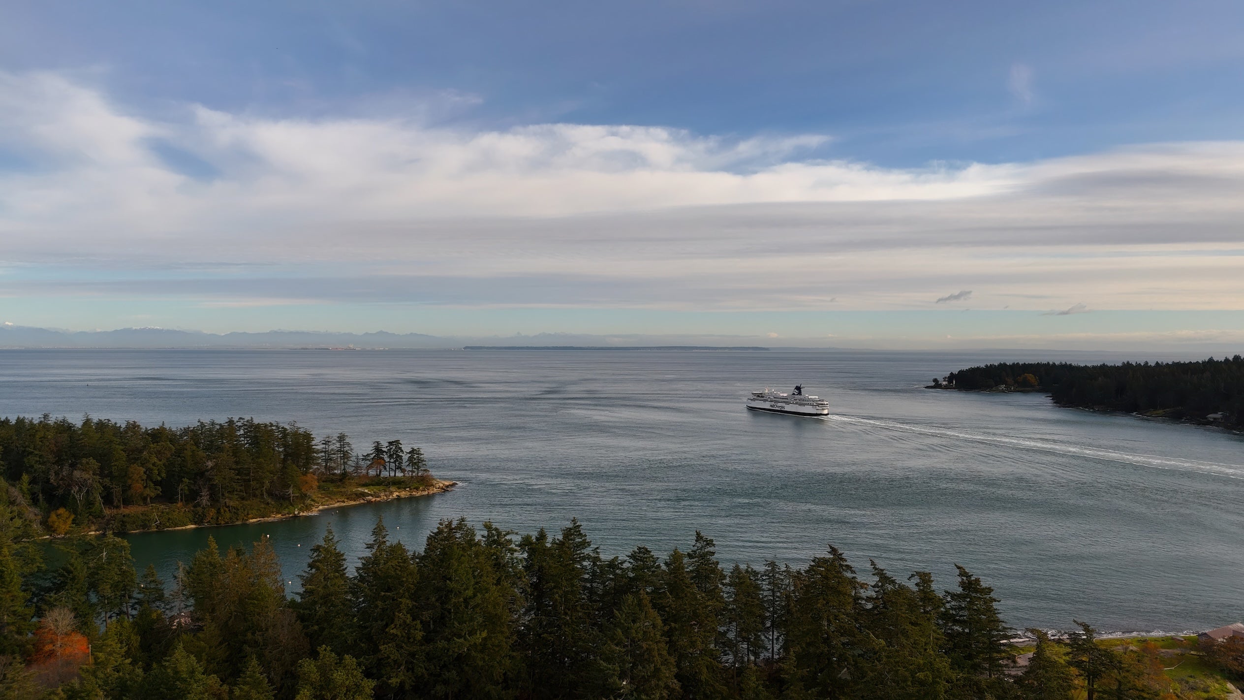 A BC ferry traveling between islands in the ocean with a big blue and cloudy sky.