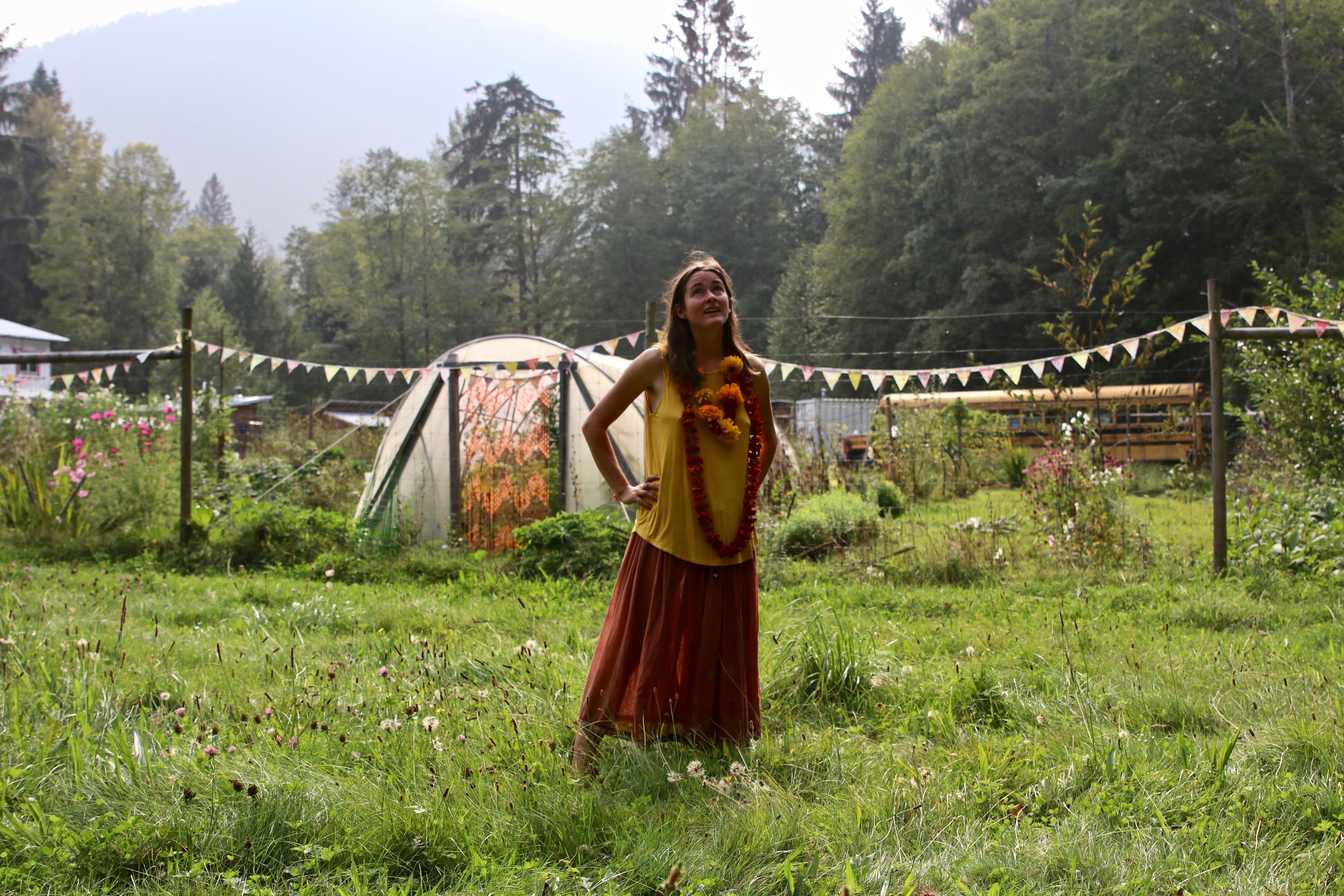 A woman in a flow dress standing in a field with a garden in the background