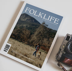 Magazine titled 'Folklife' with a person and dog on a mountain landscape, next to a camera.