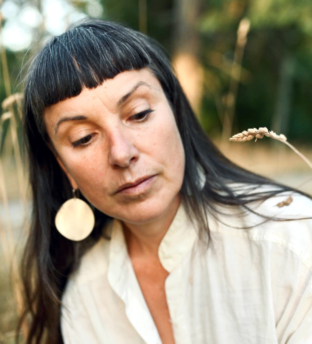 Woman with dark hair and earrings in a natural setting