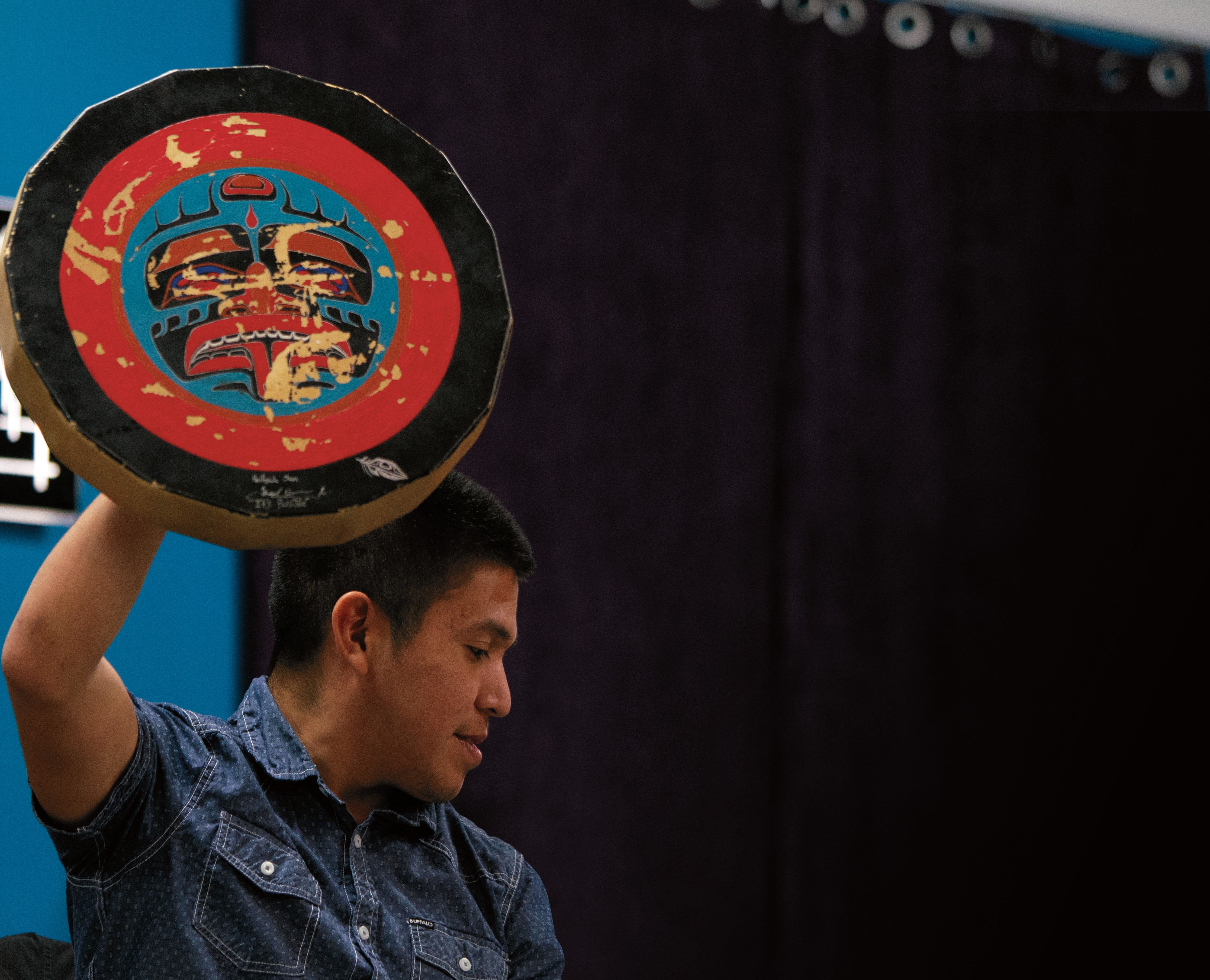 Patrick Aleck holding up a hand drum painted with a traditional formline design