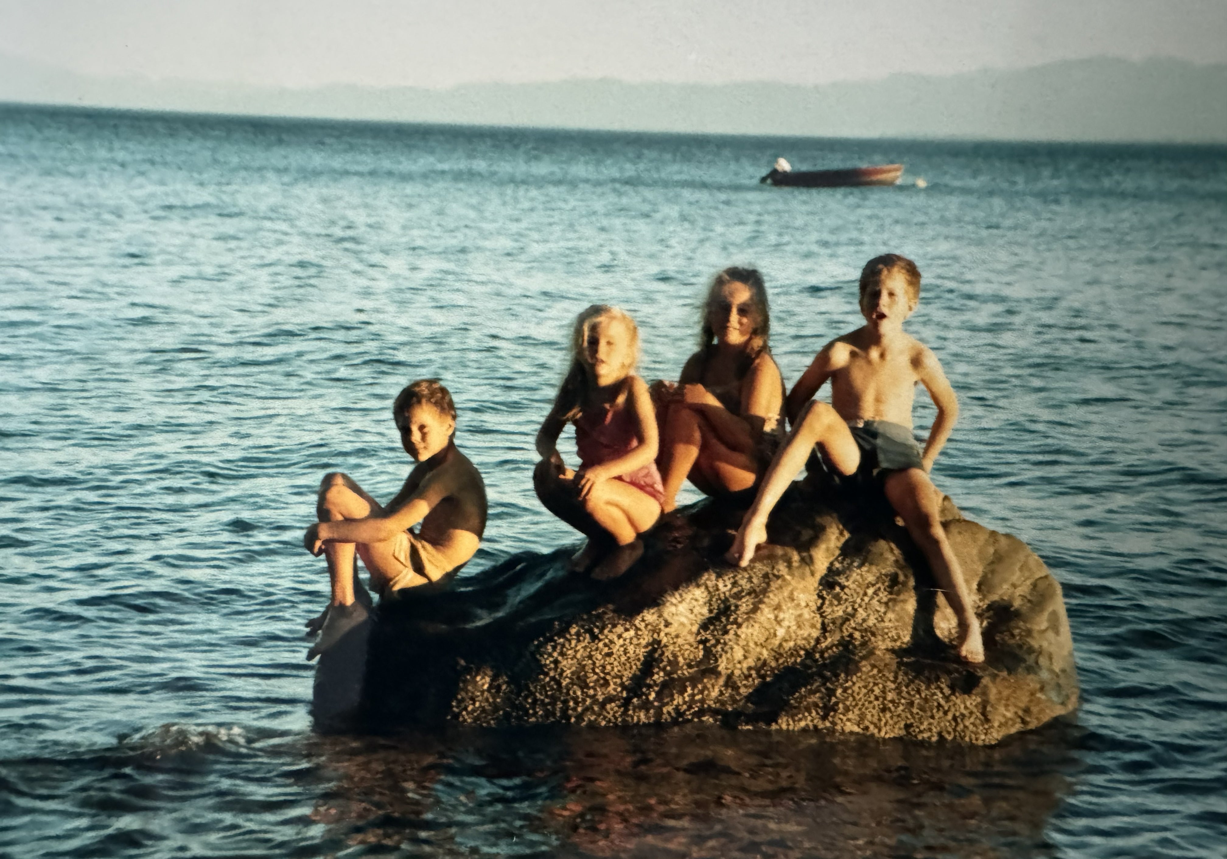 Vintage photo of four children sitting on a large rock in the ocean