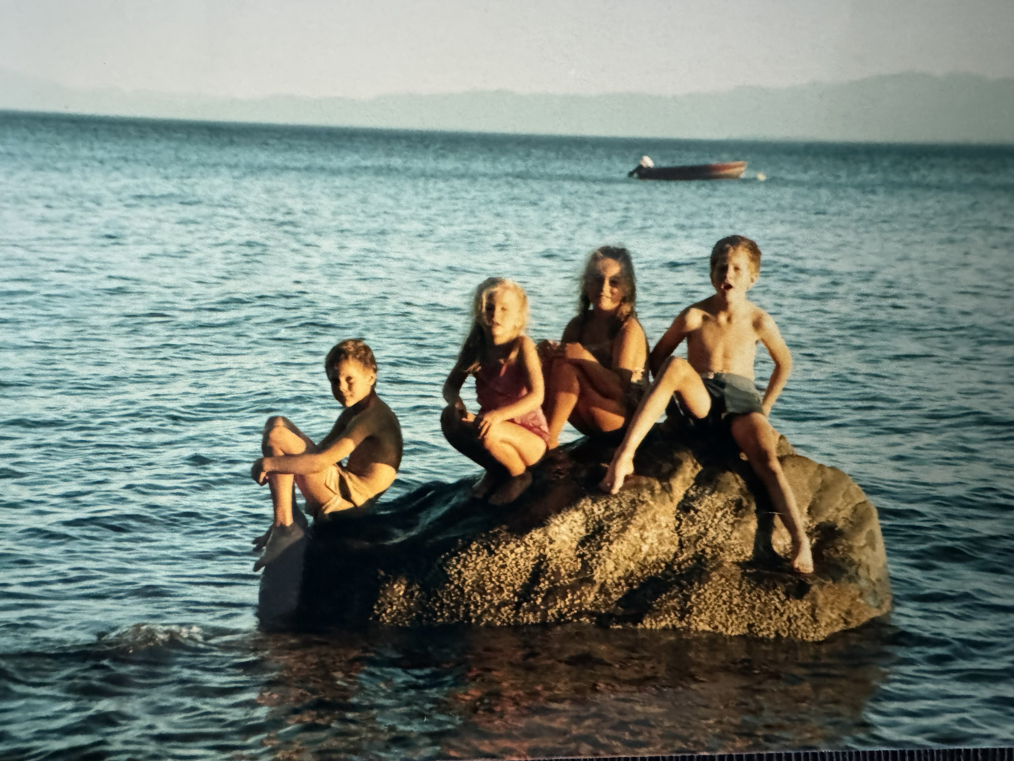 Vintage photo of four children sitting on a large rock in the ocean