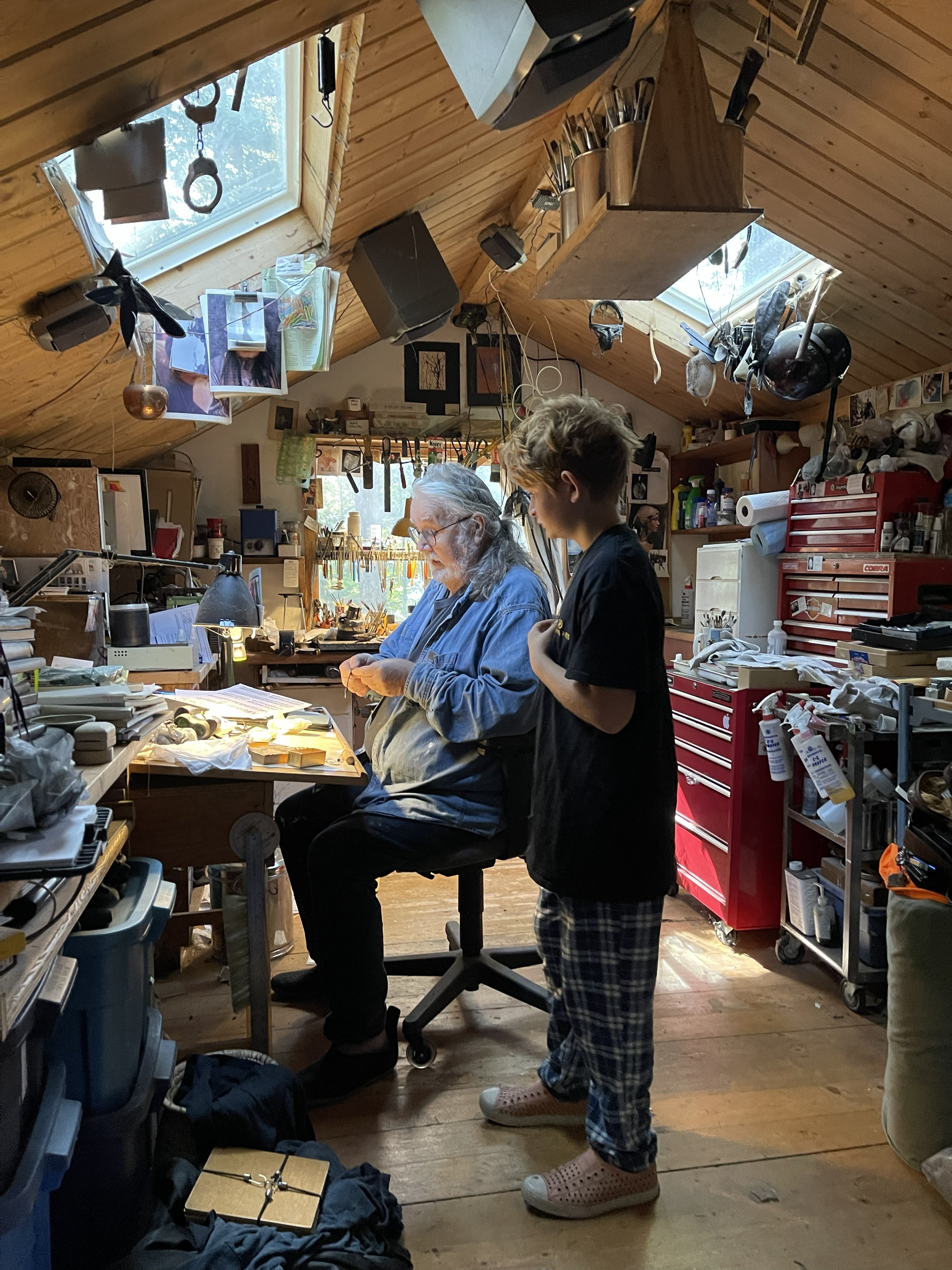Grandfather working at his studio bench while his young grandson watches beside him