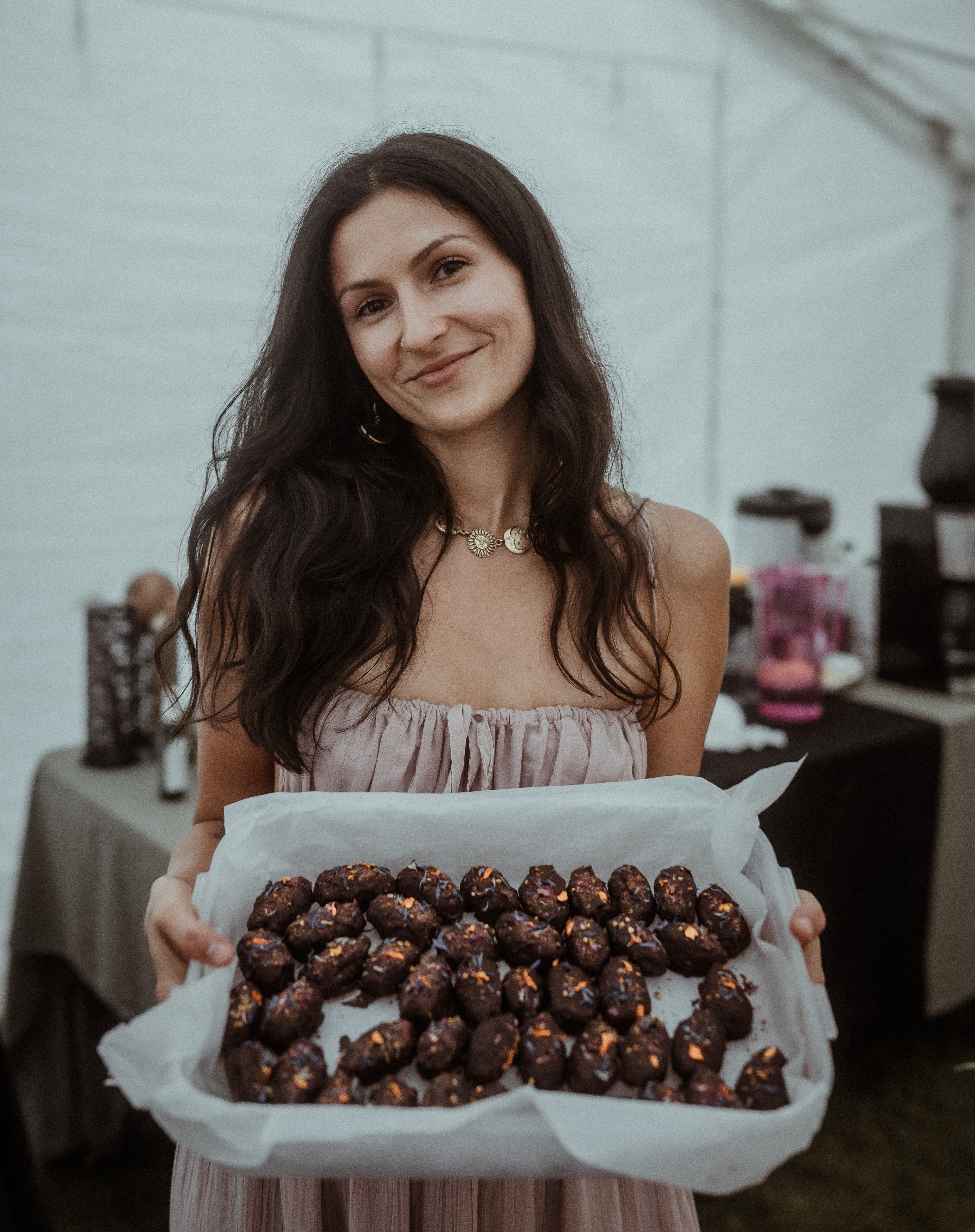 Woman in flowing dress holding parchment-lined tray of chocolate energy bites garnished with dried flowers