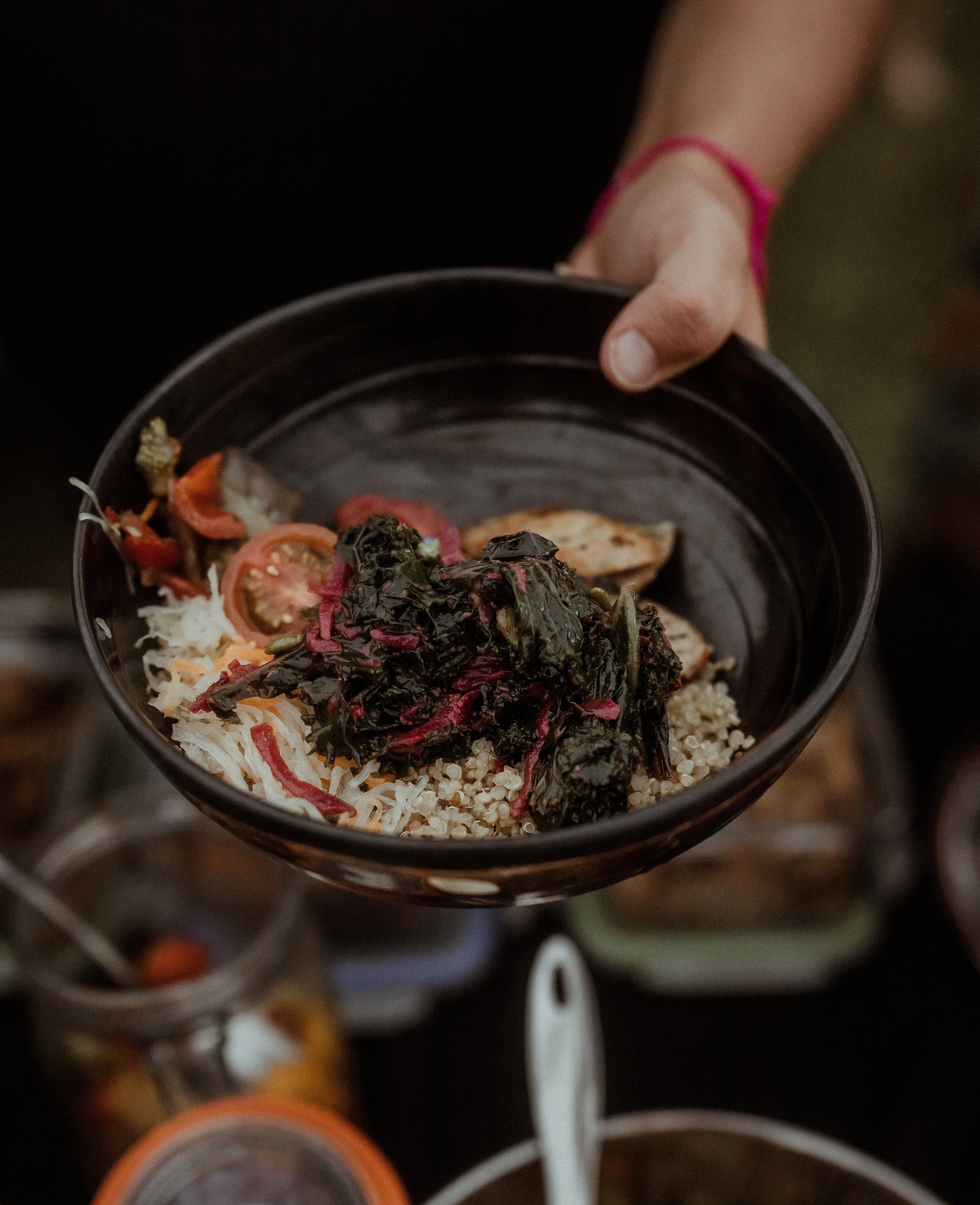Hand serving dark bowl of quinoa grain bowl topped with kale, roasted vegetables, and pickled onion