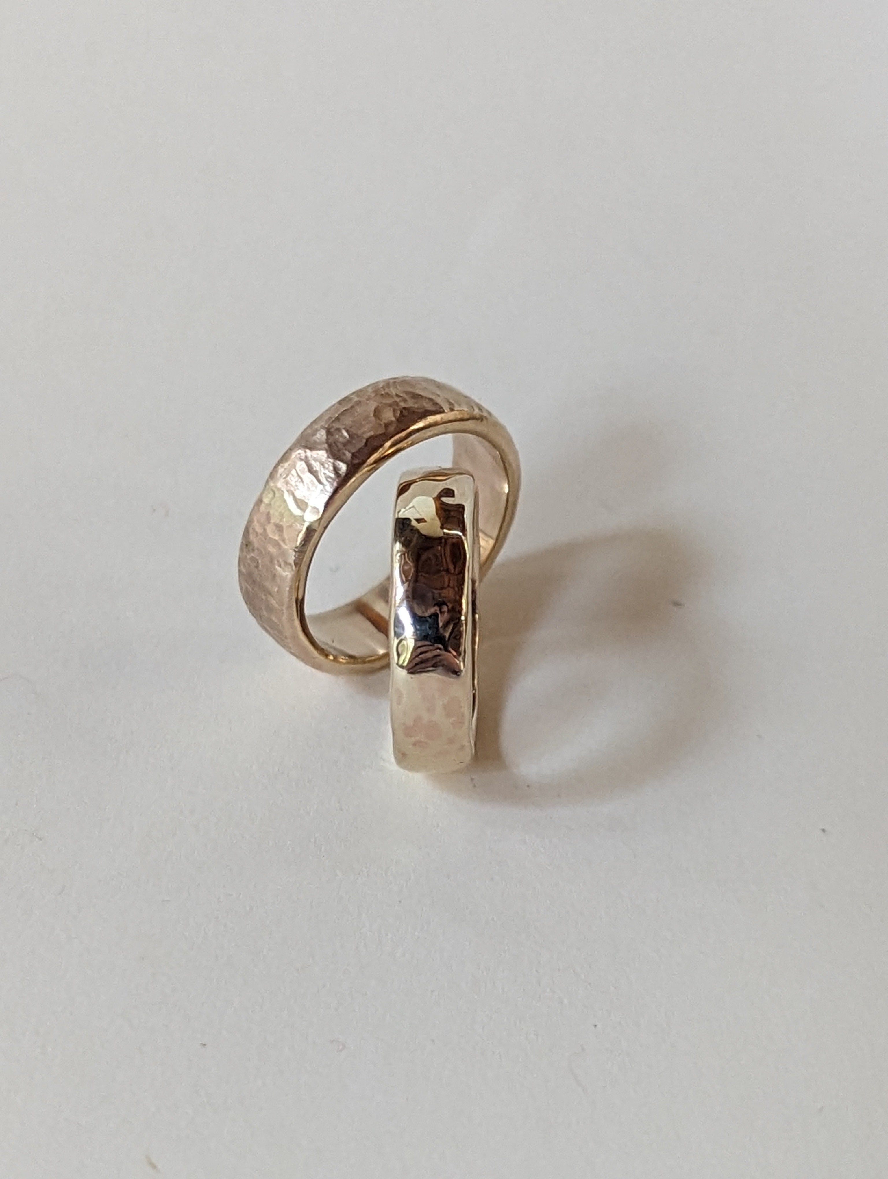 A hammered gold ring with a textured, organic surface finish, displayed on a plain light gray background.