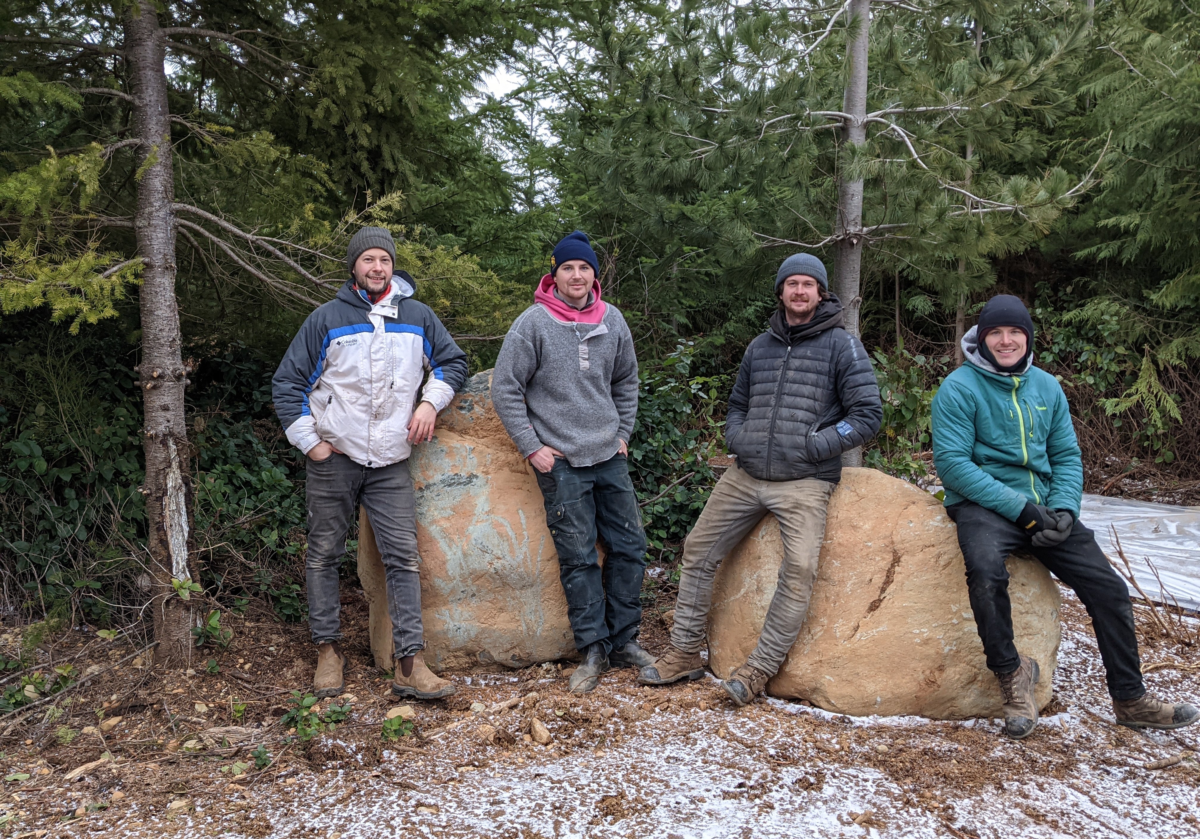 Four people posing together in a forest with large rocks and trees in the background.