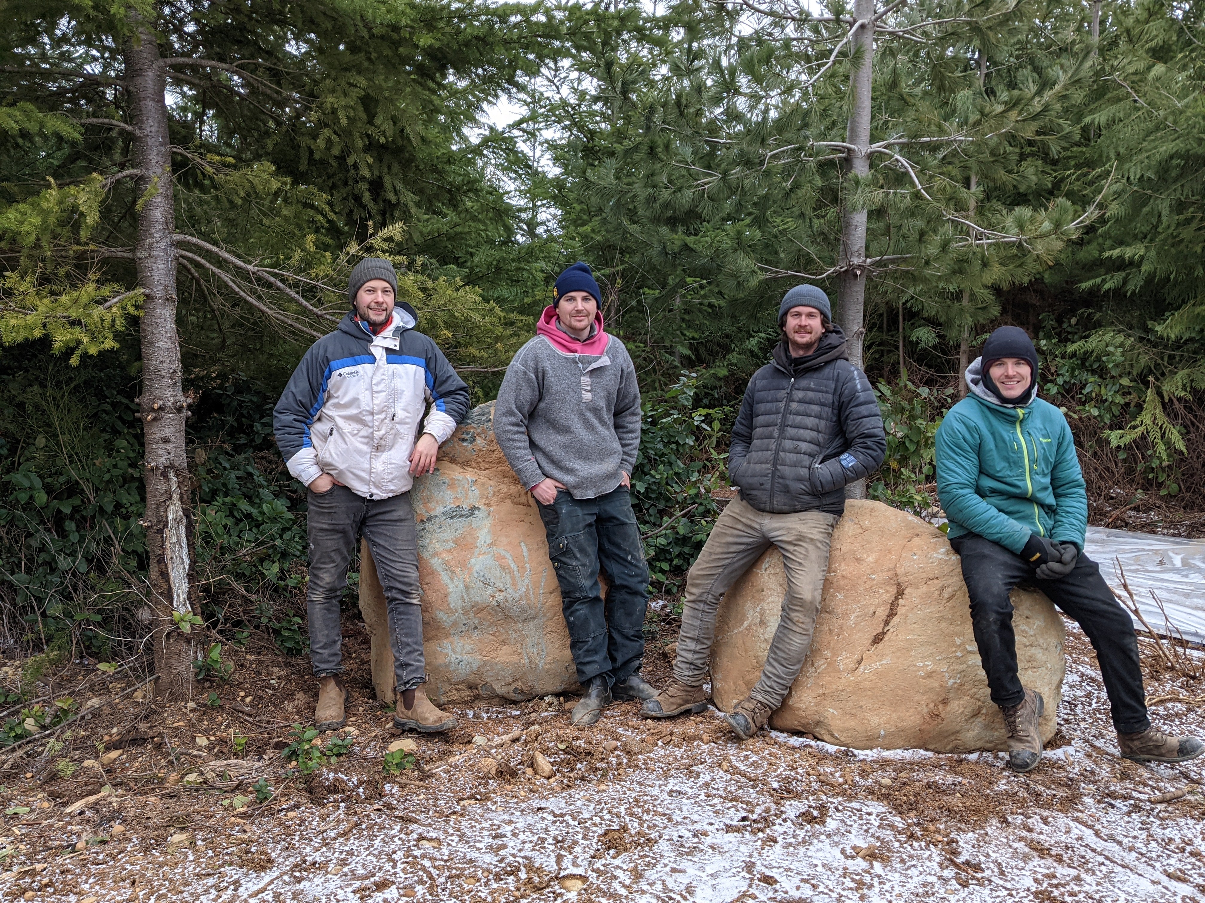 Four people posing together in a forest with large rocks and trees in the background.